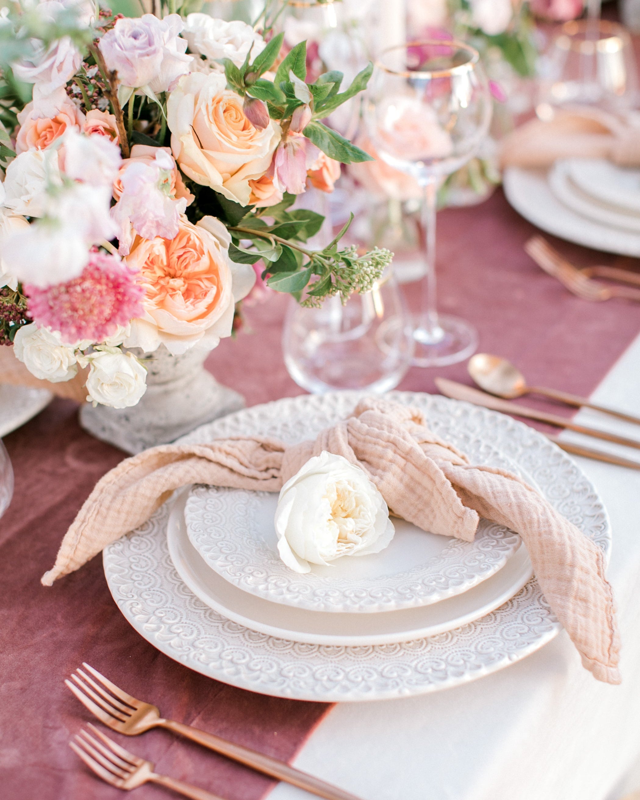 Elegant table setting with floral centerpiece, plates, and cutlery on a pink tablecloth featuring borrowed BLU's Organic Cotton Napkin in Nude.
