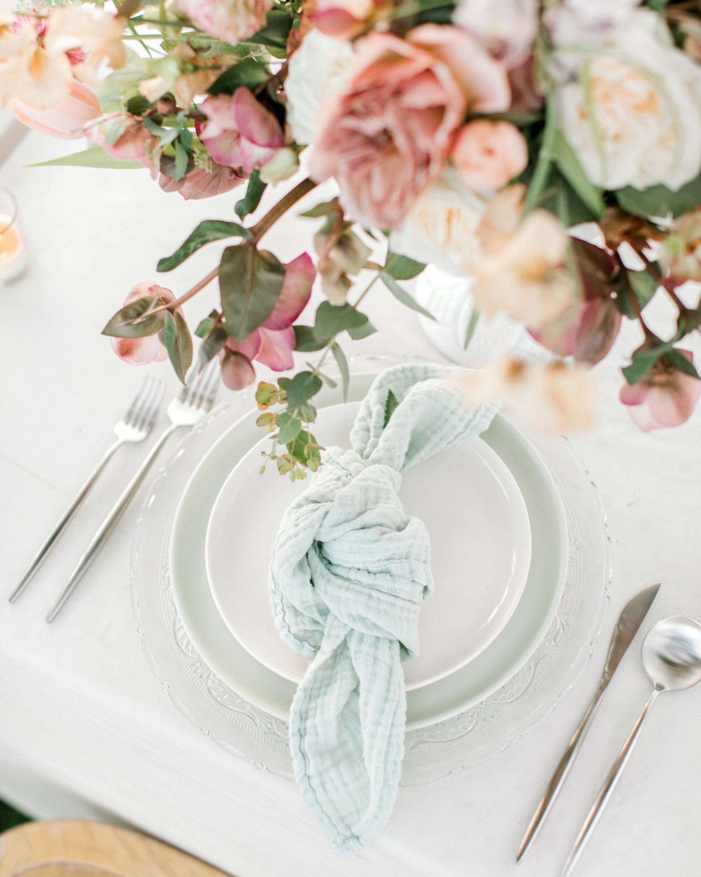 Table setting with flowers, plates, and cutlery on a white tablecloth featuring borrowed BLU's Organic Cotton Napkin in Sage.