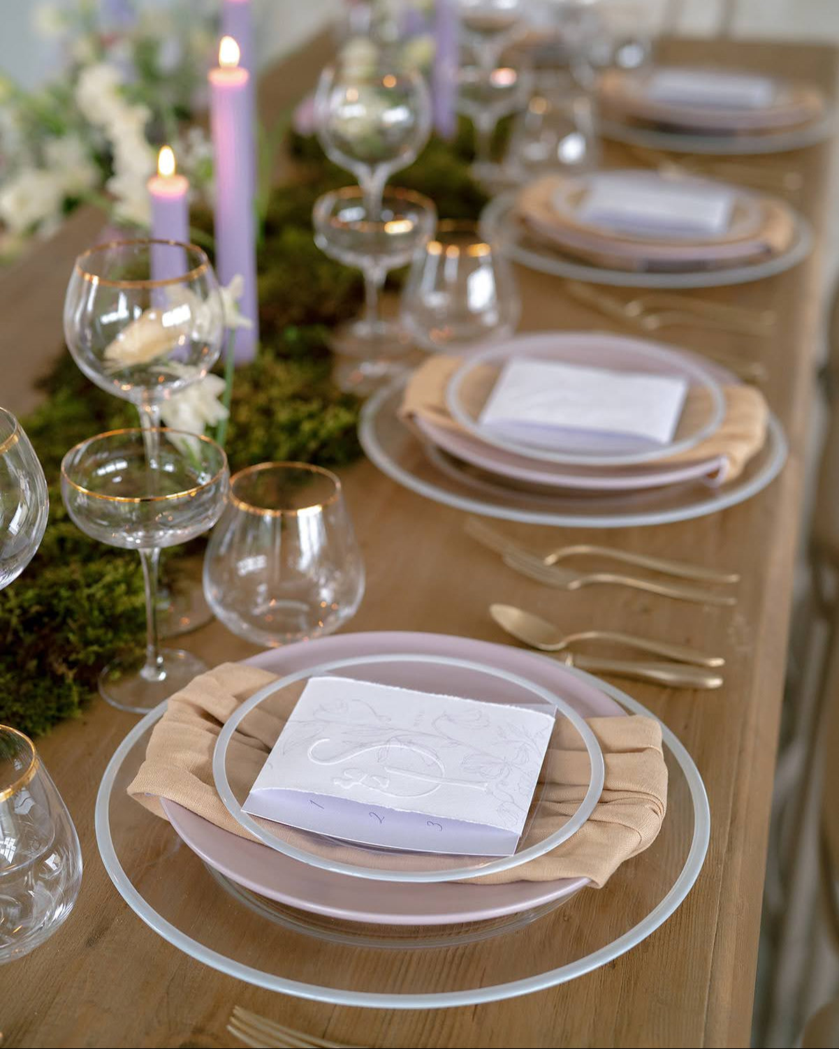 Elegant table setting with clear with gold rim Siren glassware, Siren Dinnerware with whit rim plates, and purple candles, featuring borrowed BLU's Stone Washed Linen Napkins in Nude.